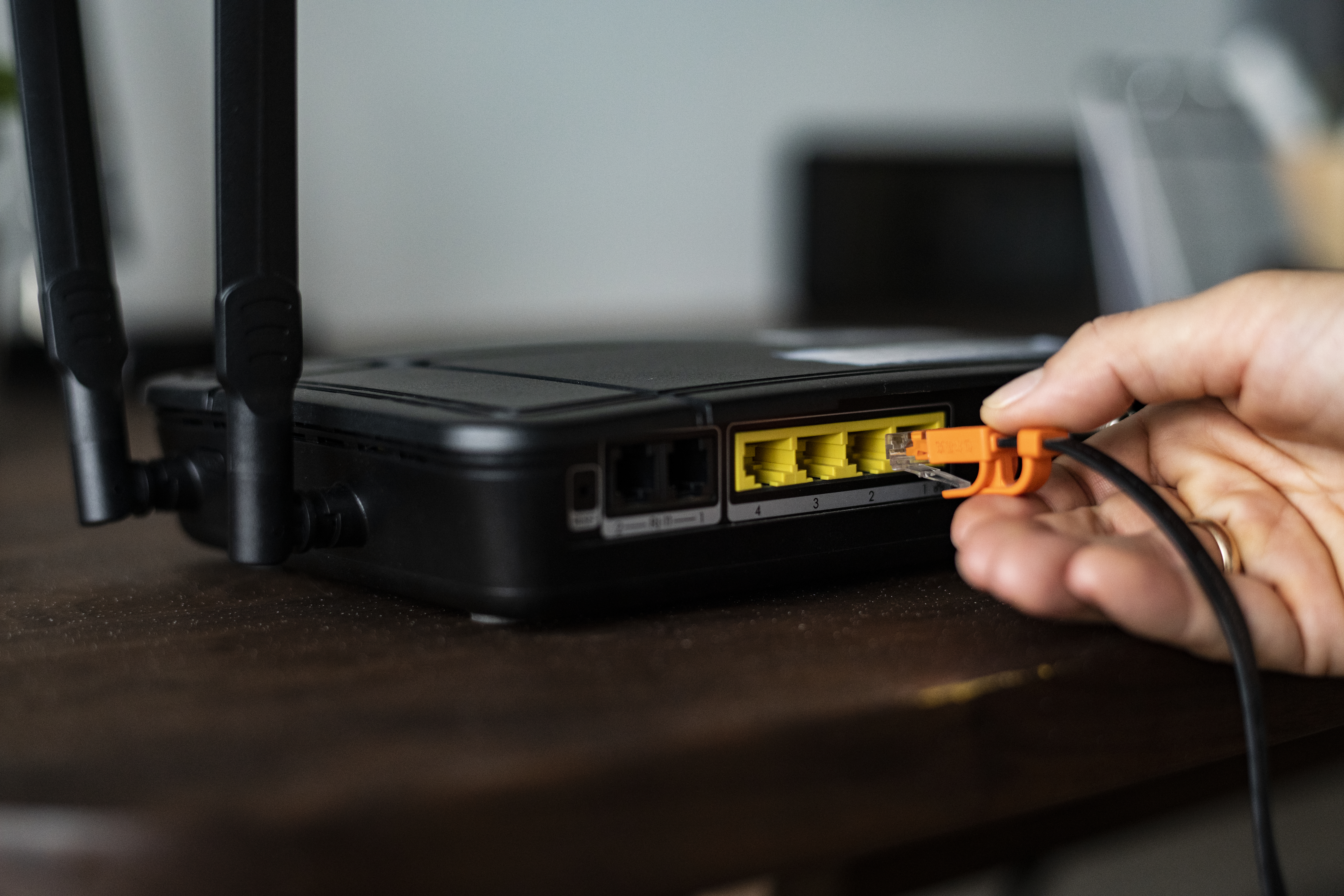 Man plugging in an ethernet cable to a wireless router as an illustration for cara merestart router Wi-Fi.