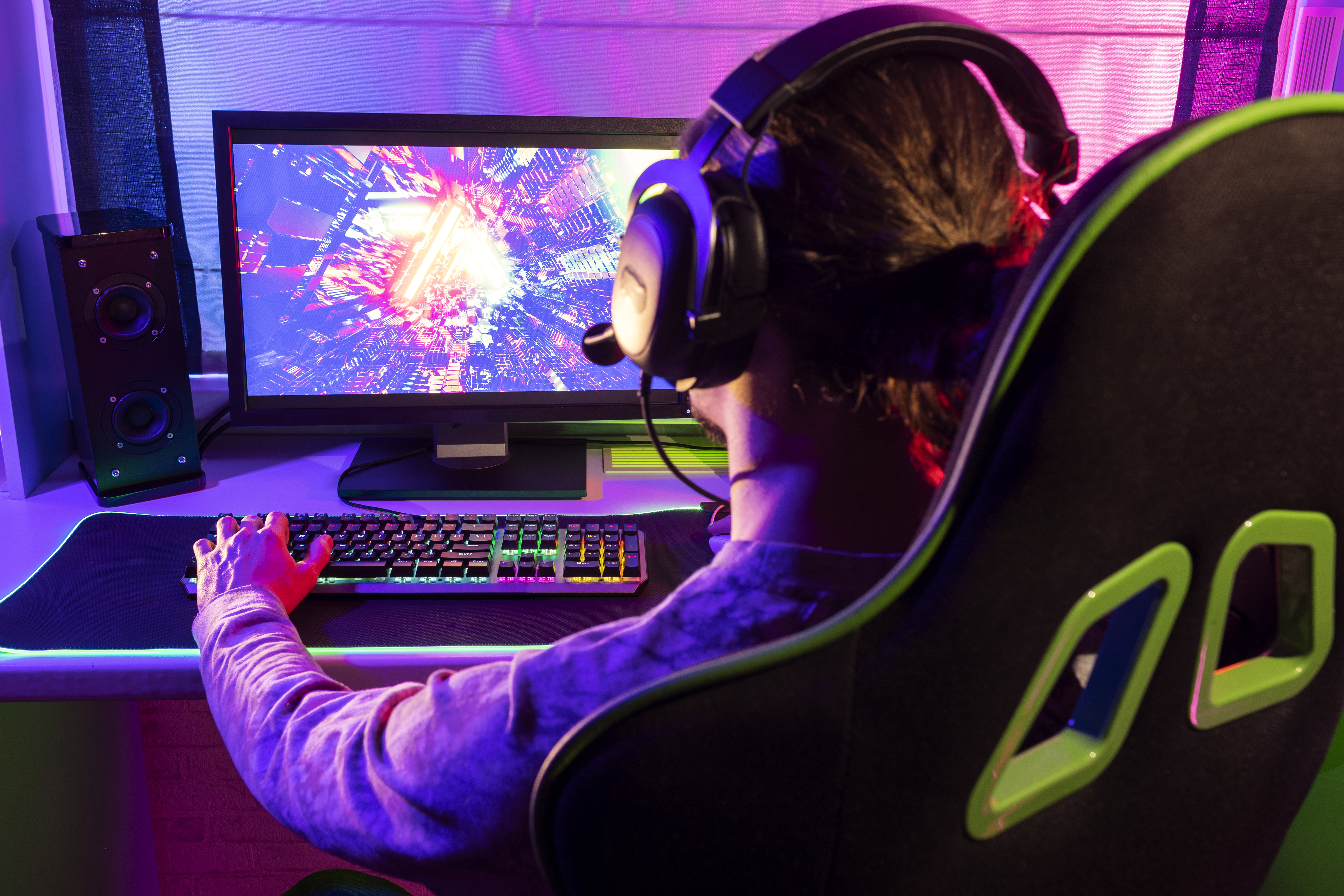 "Side view of a gamer intensely playing on a PC indoors, representing the experience of enjoying top-rated PC games (game PC terbaik).