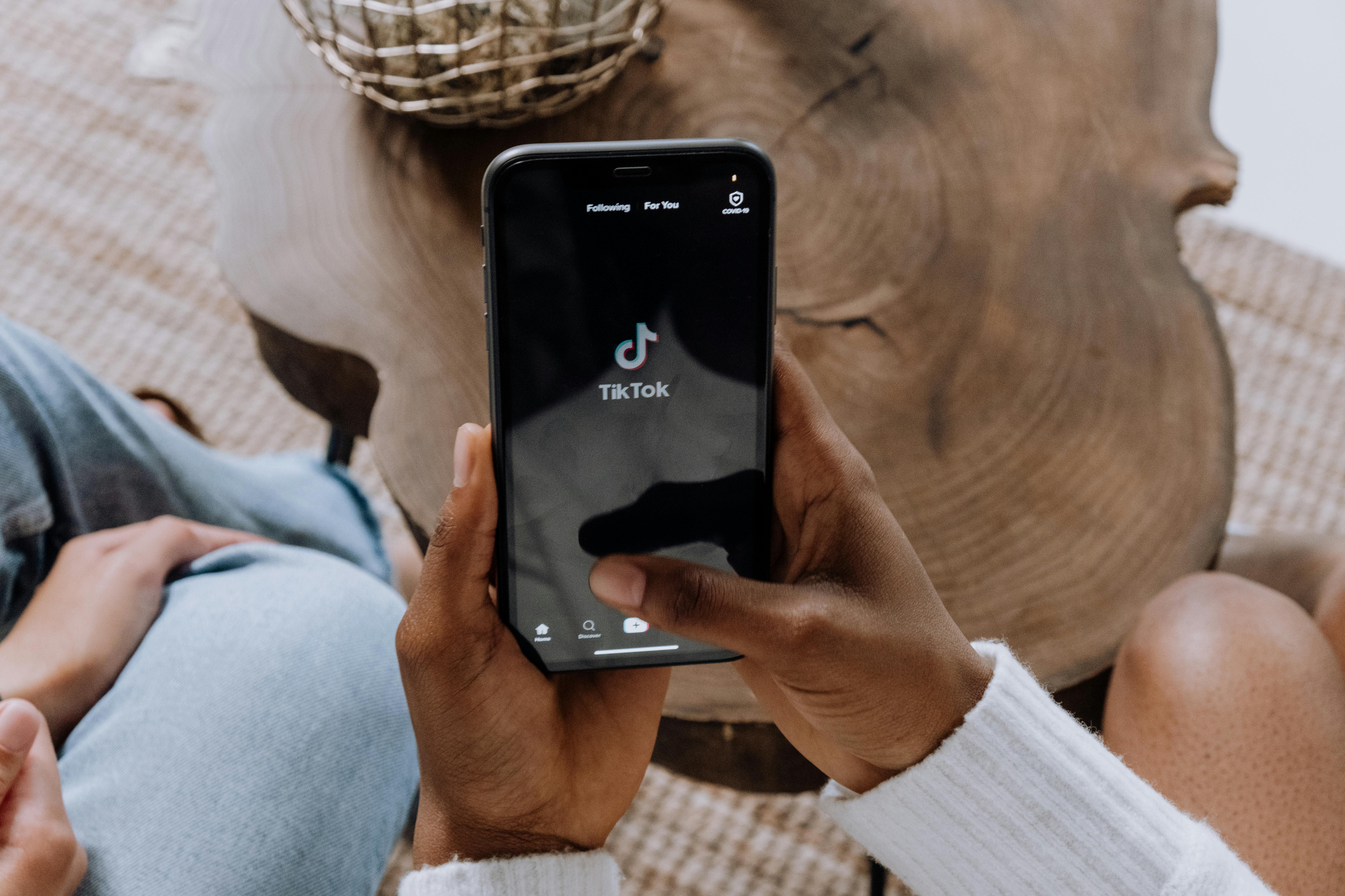 Person holding a black Android smartphone displaying the TikTok logo, illustrating the concept of downloading TikTok videos without a watermark (download video TikTok tanpa watermark).