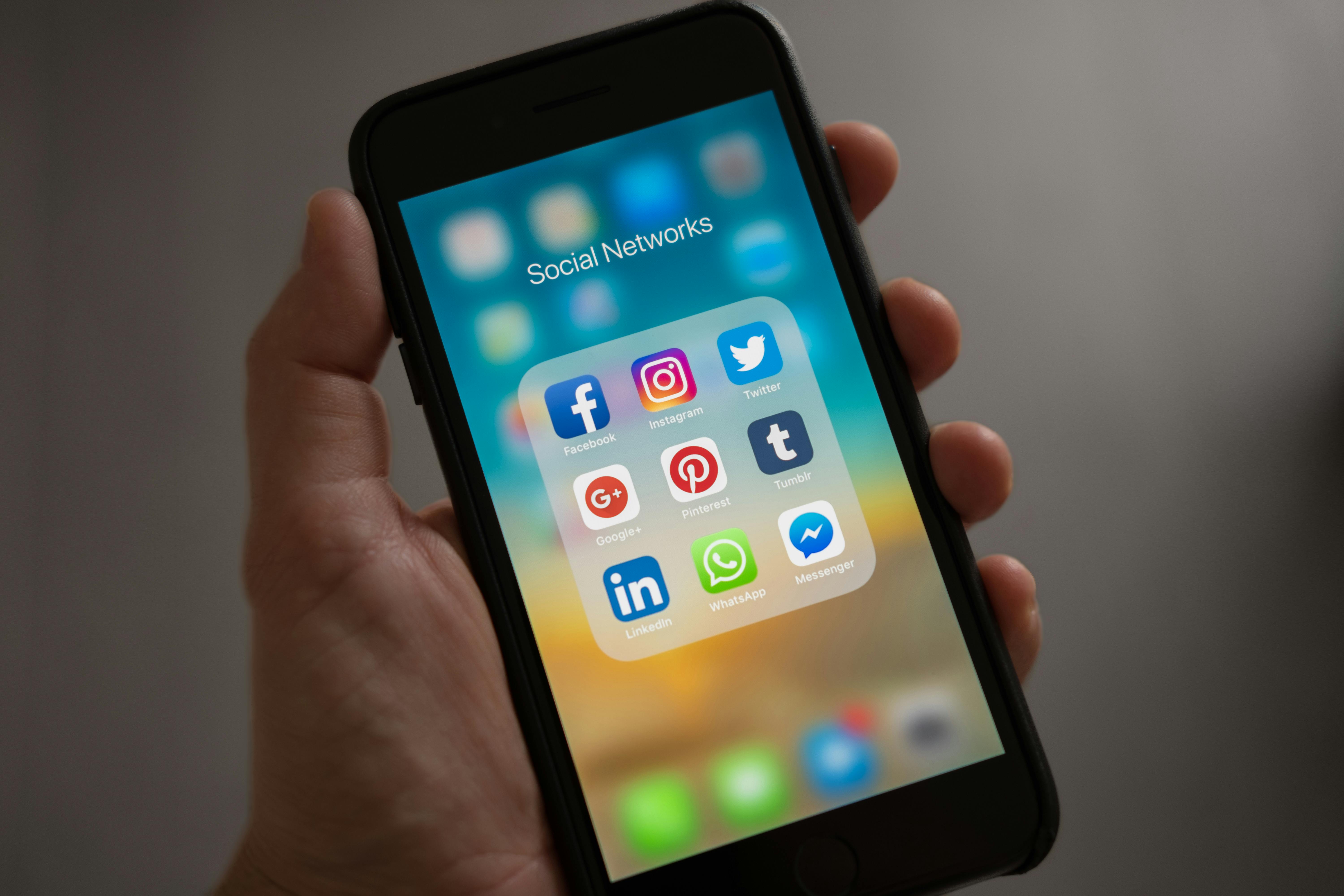 A person holding a smartphone showing several social media applications, including Pinterest, as an illustration on downloading a video from Pinterest (download video Pinterest).
