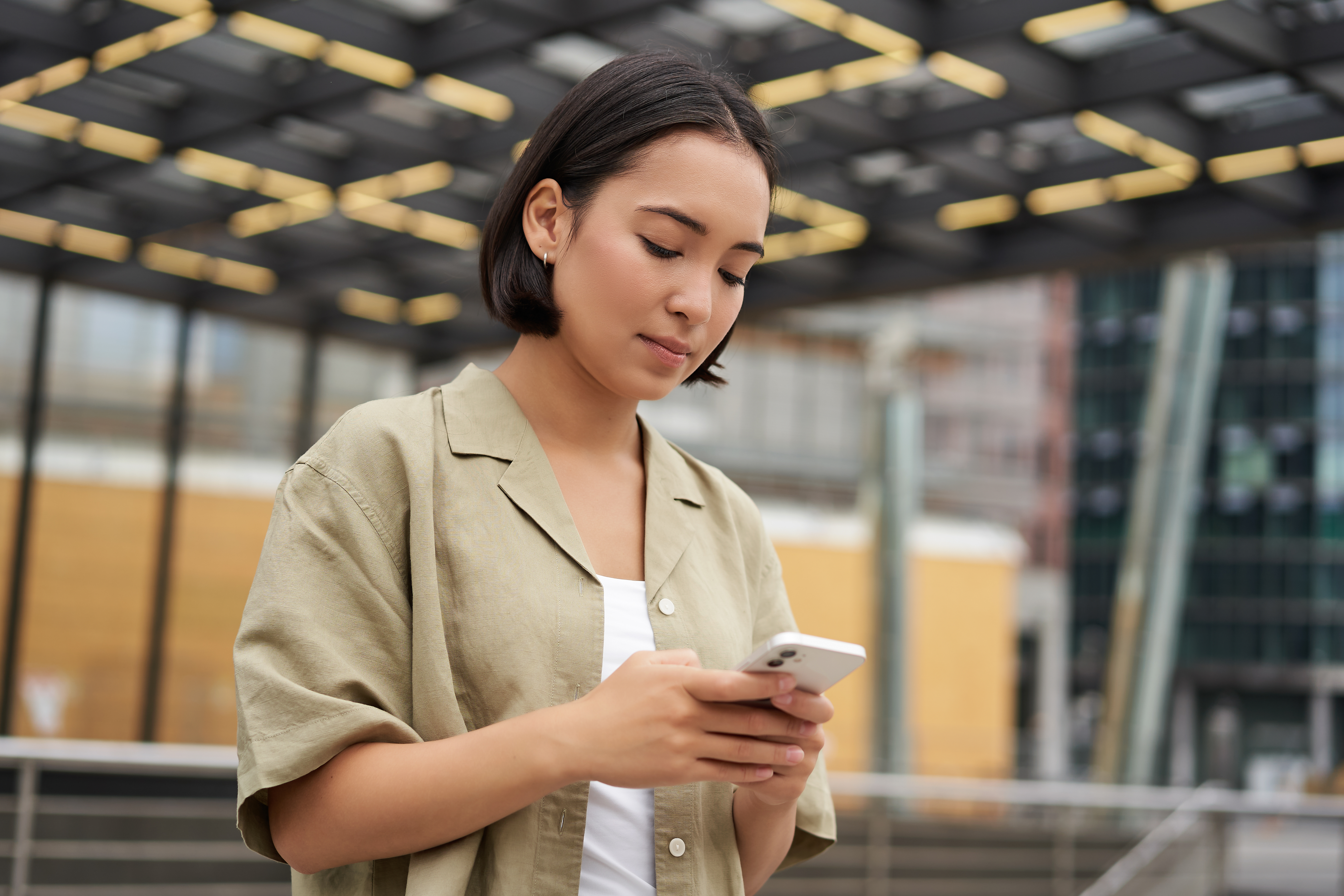 Young Asian woman standing on the street, holding a smartphone and using a mobile app, illustration for checking iPhone warranty (cek garansi iphone).