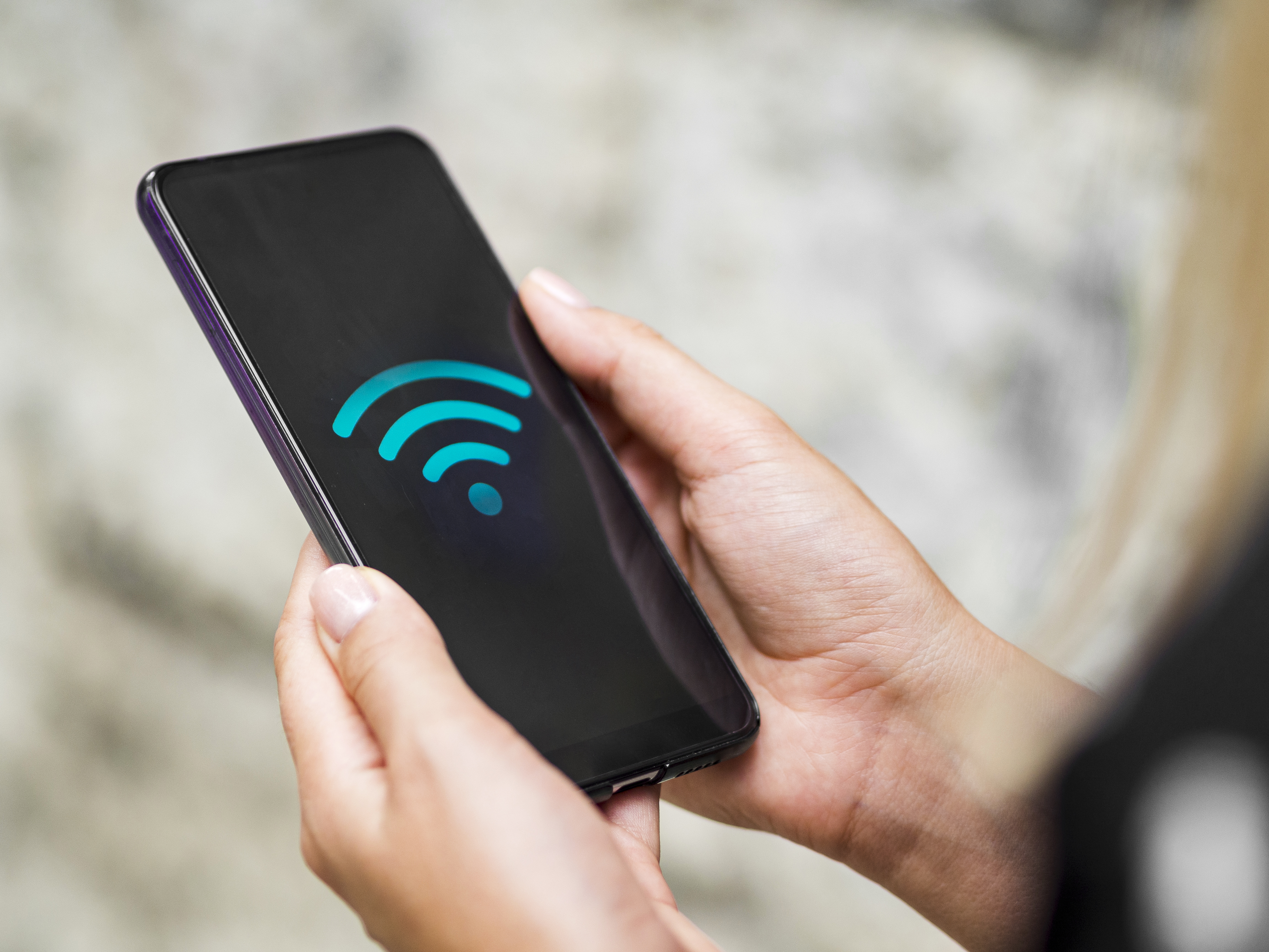 Close-up of hands holding a phone displaying a WiFi symbol, representing strong internet connection in Surabaya (WiFi terbaik Surabaya).