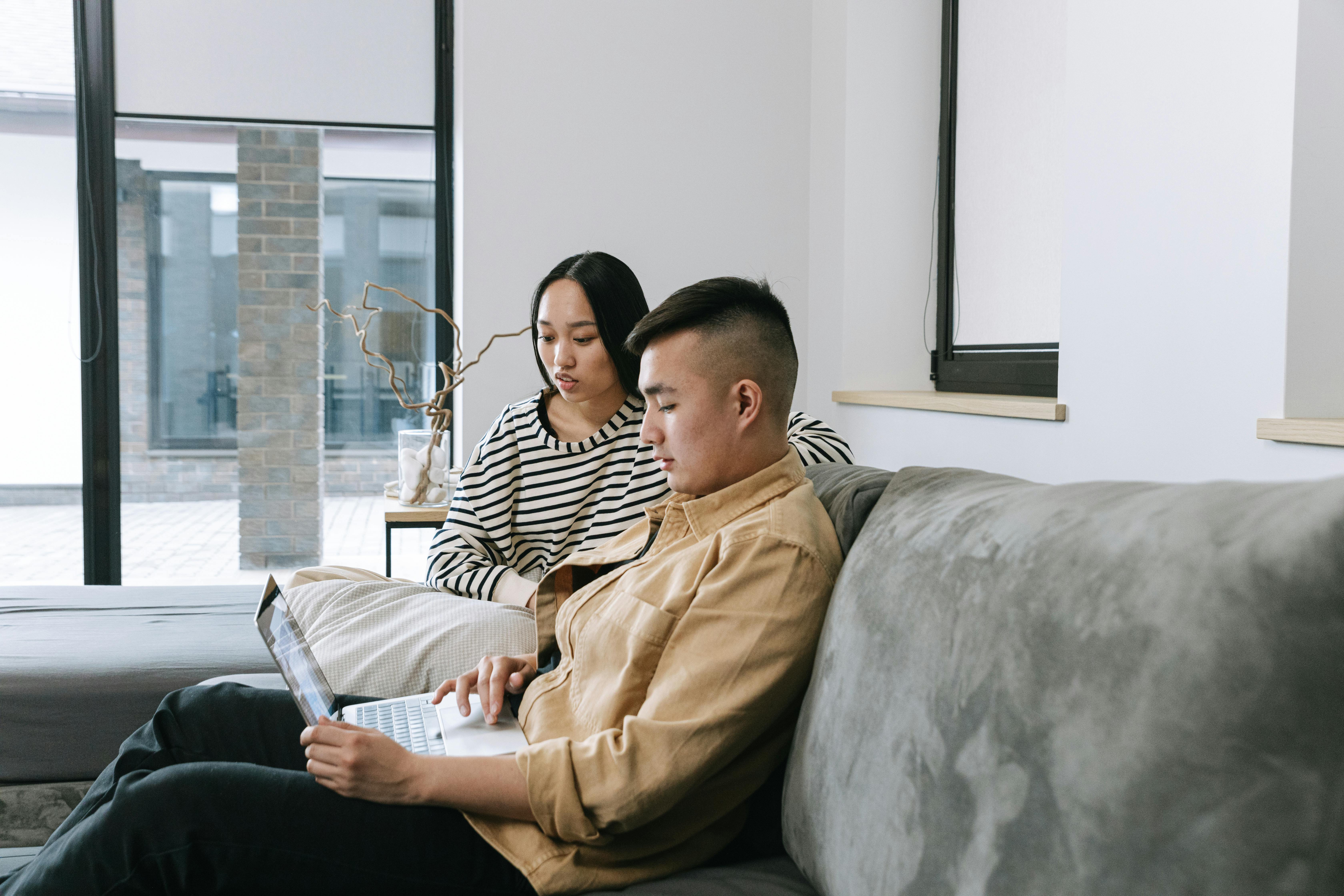 A man and a woman using a laptop on the couch, representing reliable high-speed internet service in Jakarta for home use (provider internet terbaik di Jakarta).