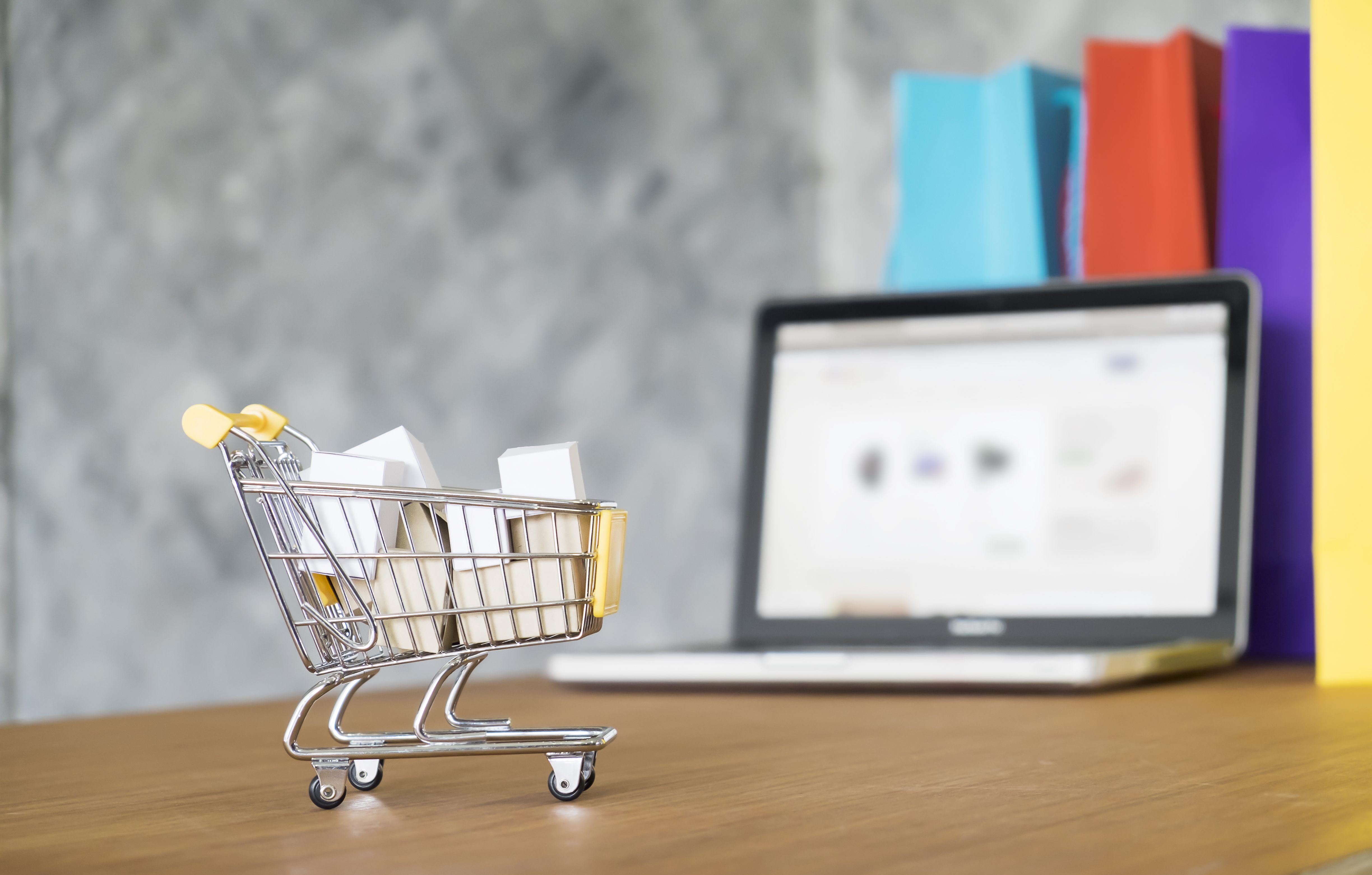 Miniature cart with packages in front of laptop illustrating online business opportunity (peluang bisnis online).
