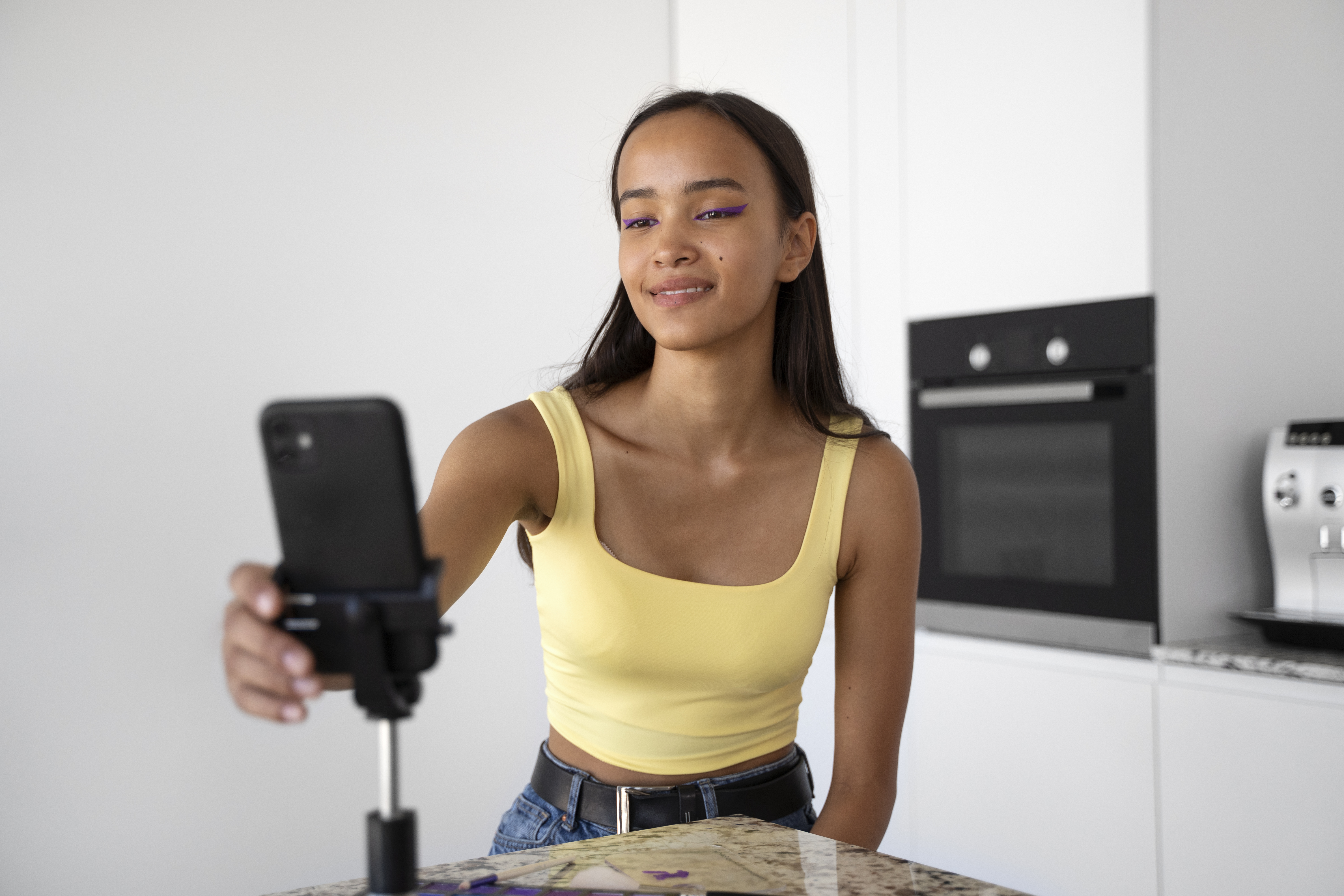Medium shot of a smiling girl in a yellow tanktop recording a video, as an illustration for how to apply for TikTok Affiliate.