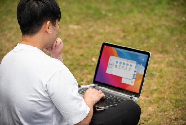 A male college student studying outdoors with a laptop on his lap, representing someone searching for or practicing how to record on a laptop (cara screen record di laptop).