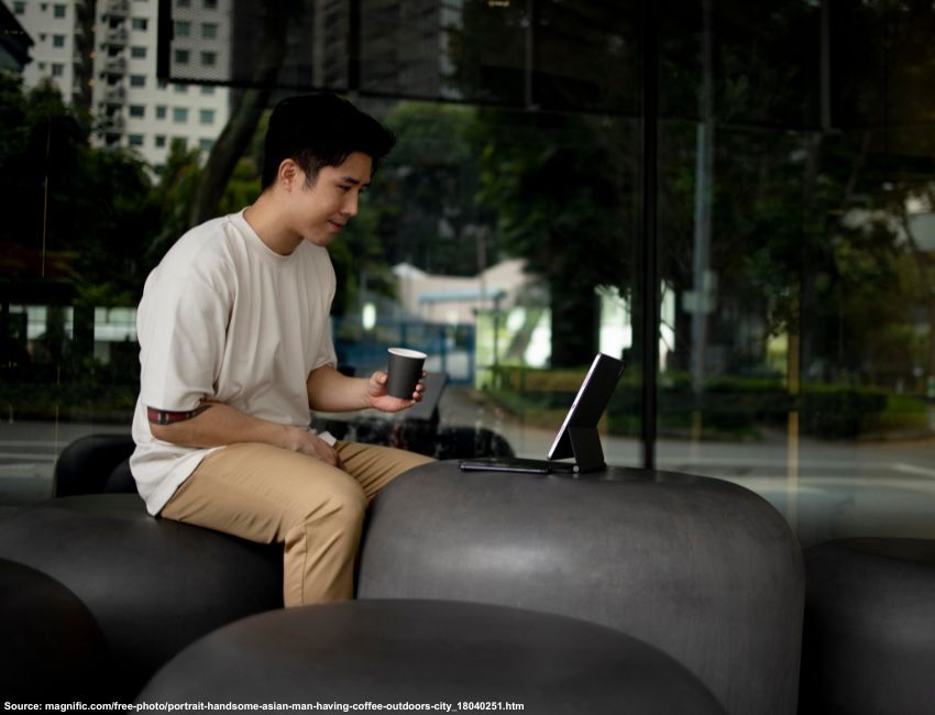 Asian professional working on a tablet with a keyboard outdoors, representing a flexible digital lifestyle.